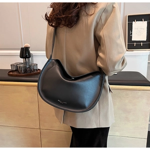 Close-up of minimalist black matte leather crescent bag worn with a beige suit