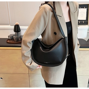 Detail view of stylish black leather half-moon shoulder bag worn by a model in soft indoor light