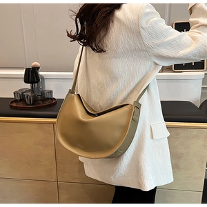 Detail of khaki leather crescent tote bag worn by model in a modern indoor setting