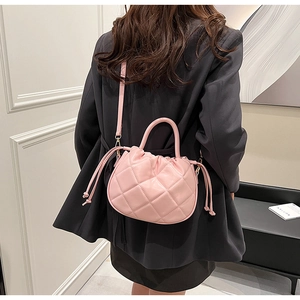 Pink quilted bucket bag with drawstring closure shown against a black blazer outfit