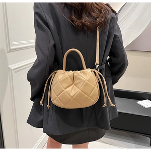 Detailed back view of a beige quilted bucket bag with drawstring closure on a shoulder strap