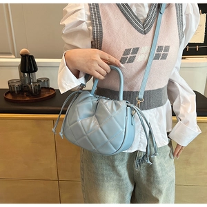 Detail of light blue quilted bucket bag with drawstring closure and gold metal chain strap
