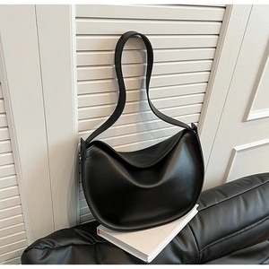 Close-up of a glossy black crescent hobo bag resting on white books in a minimalist setting