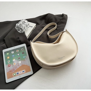 Close-up of cream half-moon tote bag with silver logo detail on smooth matte leather