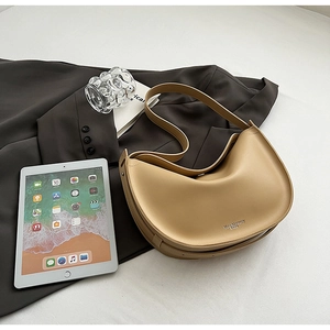 Flat lay of a beige hobo bag on a dark blazer with an iPad and glass accessory