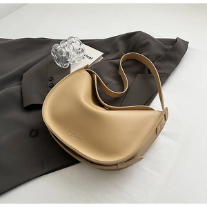 Close-up of beige crescent shoulder bag with wide strap on a dark blazer background