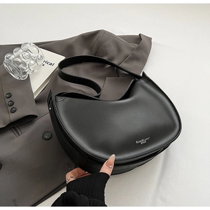 Close-up of black matte crescent tote bag with silver logo on grey blazer