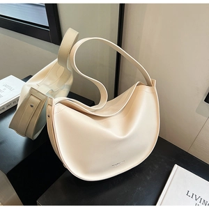 Detail of minimalist beige faux leather half-moon shoulder bag on a glossy surface