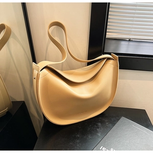 Close-up of a minimalist beige leather crescent bag on a dark table with window light