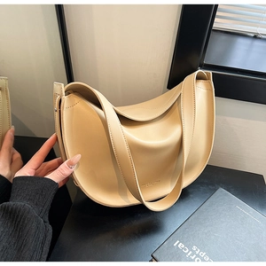 Detail of minimalist cream leather crescent bag with wide strap and gold logo