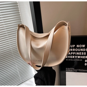 Detail of minimalist cream half-moon shoulder bag held by a model in modern urban setting
