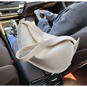 Detailed macro view of cream half-moon tote bag with minimalist logo on car leather seat