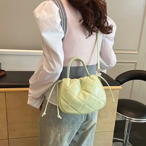 Pale green quilted bucket bag with drawstring and adjustable strap shown on model