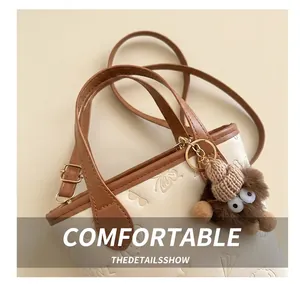Detail of cream bucket bag with brown trim, embossed texture, and plush monster charm