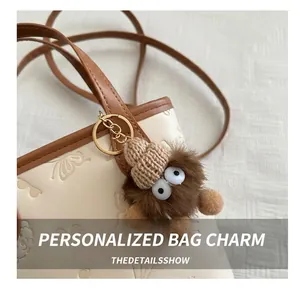 Close-up of a brown fluffy plush charm with big eyes on a cream leather bucket bag