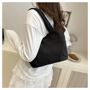 Minimalist black canvas tote bag with wide strap shown in a lifestyle casual outfit