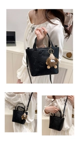 Detail view of black embossed leather bucket bag with cute plush monster charm and shoulder strap