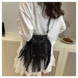 Detalle de bolso bandolera negro con flecos, remaches plateados y textura de piel granulada