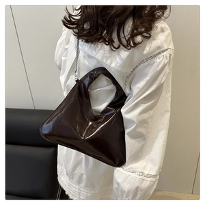 Detail of a dark brown glossy leather handbag with integrated cutout handle and metal chain