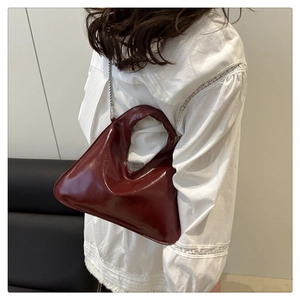 Model wearing dark red glossy shoulder bag with metal chain strap and half-moon design