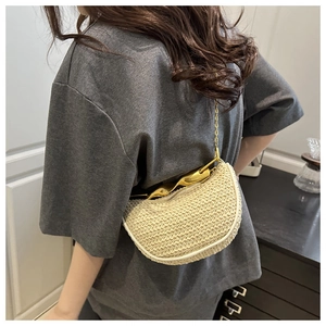 Detail view of woven crescent bag with gold handle and metal chain on model