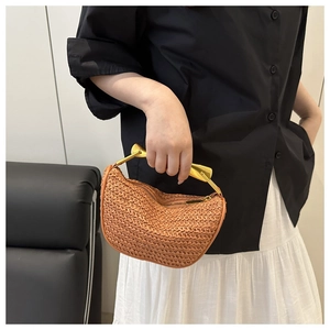 Close-up of a crescent straw bag featuring a sleek gold metal handle and woven texture