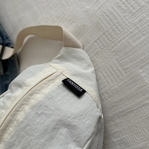Détail macro de l'étiquette FANYISSA sur un sac bandoulière minimaliste en nylon crème