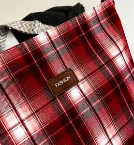 Détail du sac cabas en toile à carreaux rouges avec logo cuir et bandoulière tissée