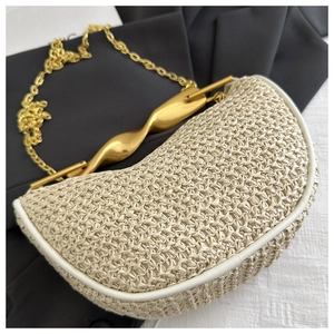 Detailed shot of crescent straw handbag featuring a twisted gold metal handle and chain