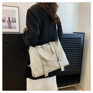 Detailed view of cream faux leather tote bag with silver rings on a model in black suit