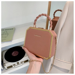 Pink box-shaped handbag with woven handle and gold metal trim shown in a home setting