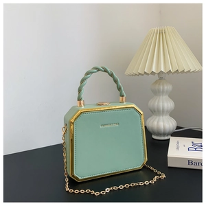Detail of light green hexagonal box bag with golden metal trim and braided top handle