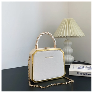 Detailed close-up of octagonal white faux leather handbag with gold metal trim and chain
