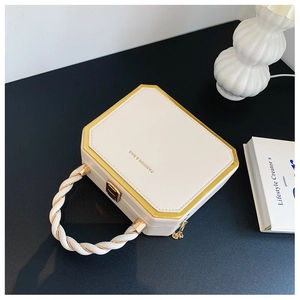 Detail of cream hexagonal hard-shell handbag with golden metal frame and woven handle