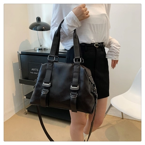Detail view of large black tote bag featuring metallic buckle straps and dual top handles