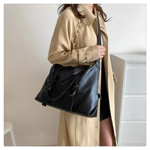 Model wearing a large black vintage tote bag in PU leather over a stylish beige trench coat