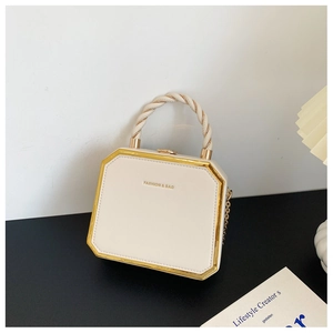 Detail of white box bag with gold metal frame and twisted handle on a modern desk