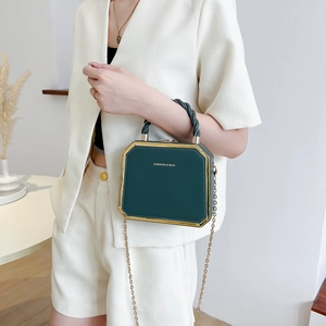 Deep green box handbag with gold frame and chain strap shown on a model in an elegant suit