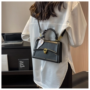 Detail of black leather square handbag with golden buckle and silk scarf handle decoration