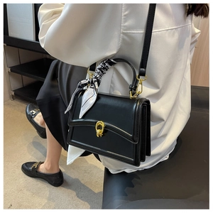 Detail of black leather handbag with golden twist lock and decorative printed silk scarf