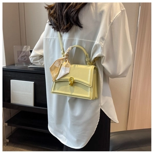 Detail of light green square handbag with decorative silk scarf handle and golden hardware