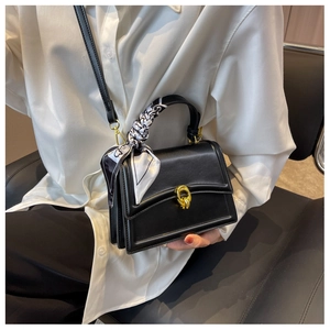 Detail of black structured crossbody bag with gold twist lock and printed silk scarf handle