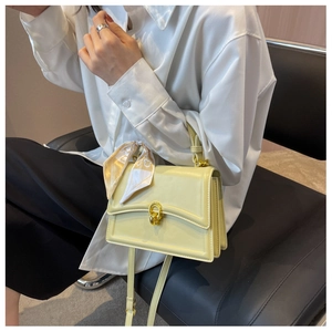 Detail of light yellow square crossbody bag featuring silk scarf handle and gold chain lock