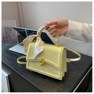 Detail of yellow crossbody bag featuring a silk scarf wrapped handle and gold hardware
