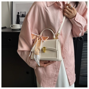 Detail of cream leather square handbag with metal clasp and decorative silk scarf accessory
