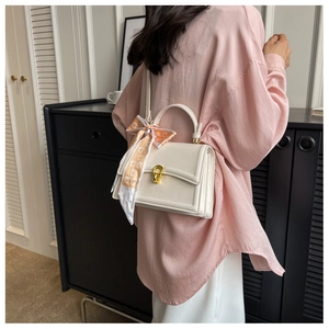 Close-up of cream square handbag with gold ring buckle and printed silk scarf handle