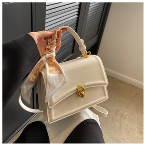Detail of cream square handbag with orange printed scarf wrapped on handle and gold hardware