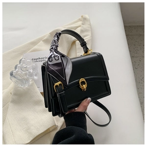 Detail of black leather handbag with gold clasp, accordion sides, and printed scarf handle
