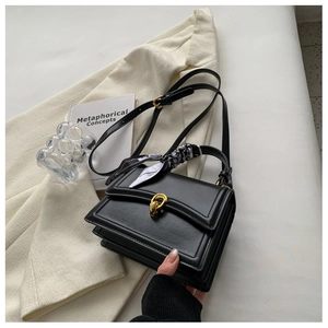 Detail of black structured crossbody bag with silk scarf handle and gold buckle