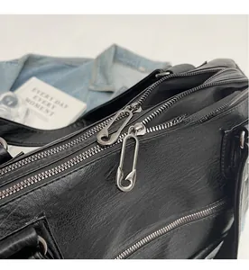 Detail of premium black lychee leather bag featuring unique safety pin zipper pullers